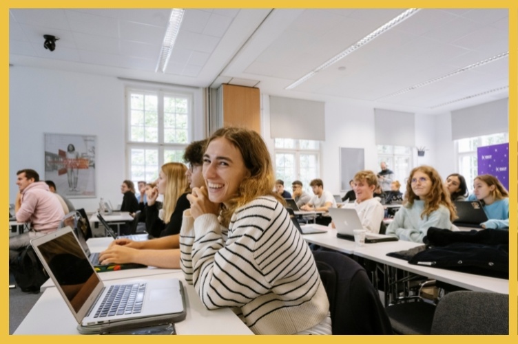 Student on a laptop in a lecture hall smiling